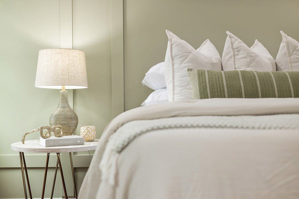 cama tendida con mesa de luz a un lado y la lámpara encendida.